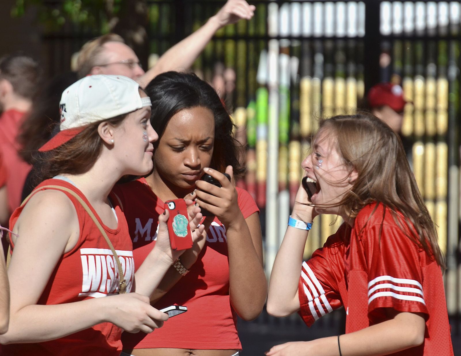 Three young women with phones phones among the crowd of Wisconsin Badgers football fans outside Camp Randall Stadium in Madison prior to the start of a game