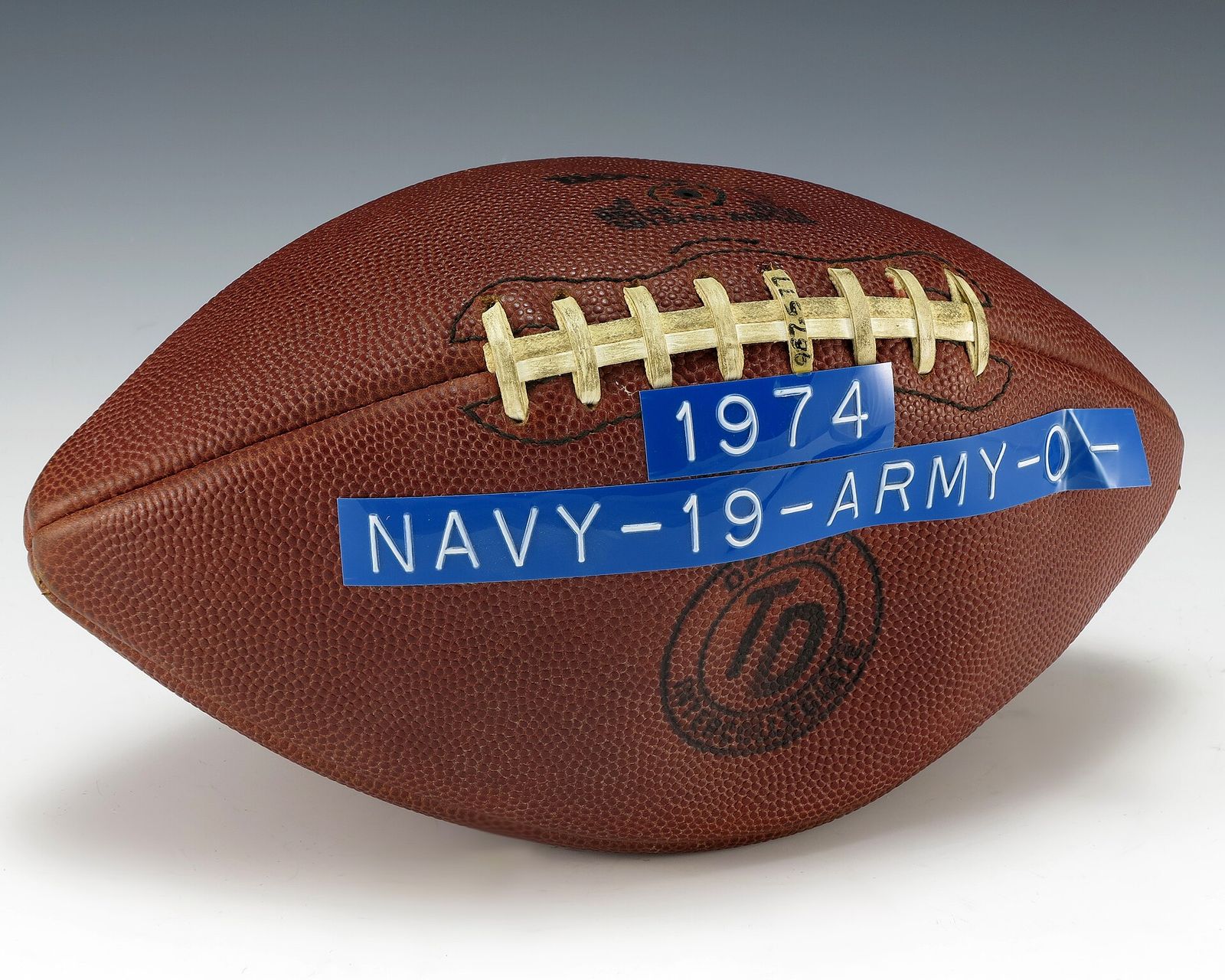 Game football used in the 1974 Army-Navy game. Adhered to the football a blue label with white lettering reveals the game’s final score (Navy 19, Army 0).